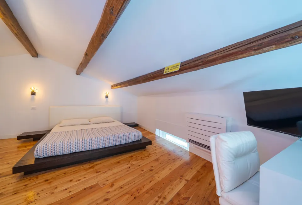 Camera in mansarda con letto basso, parquet e travi antiche